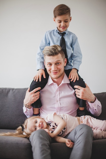 Gratis foto glimlachende vader met zoon op zijn schouders en dochter op zijn knieën
