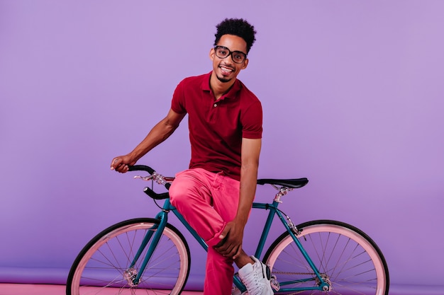 Glimlachende verlegen Afrikaanse man in roze broek poseren met fiets. knappe zwarte man geïsoleerd.