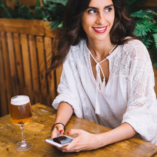 Glimlachende vrouw aan tafel met smartphone