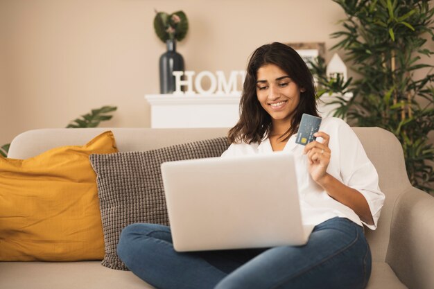 Glimlachende vrouw die aan laptop werkt en een creditcard houdt