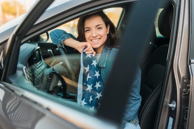 Glimlachende vrouw die de grote vlag van de VS in auto houdt