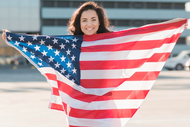 Glimlachende vrouw die de grote vlag van de VS over zich houdt