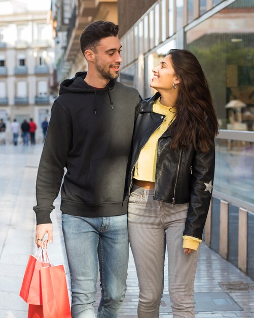 Glimlachende vrouw die de jonge positieve mens met het winkelen pakketten koestert