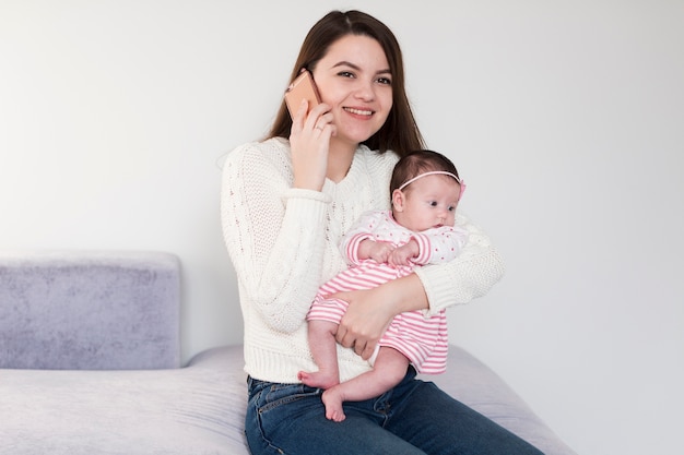 Gratis foto glimlachende vrouw die dochter en praten op telefoon