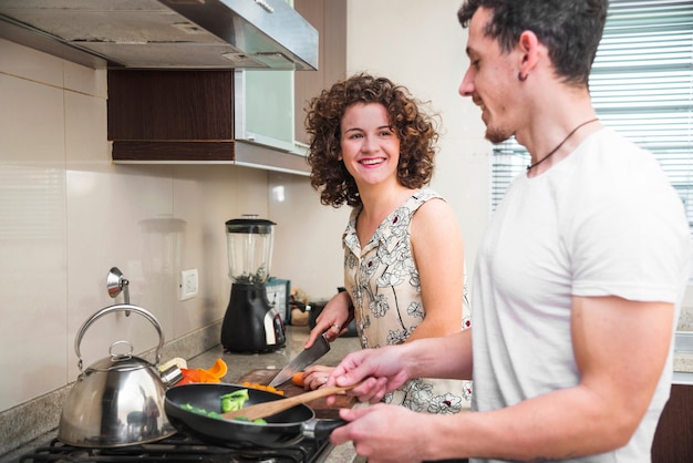 Glimlachende vrouw die haar echtgenoot bekijken die voedsel in de keuken voorbereiden