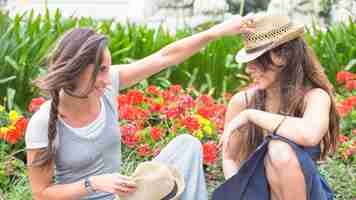 Gratis foto glimlachende vrouw die hoed over de hoedenzitting van haar vriend zetten in de tuin