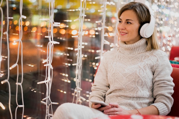 Glimlachende vrouw die hoofdtelefoons draagt dichtbij Kerstmislichten