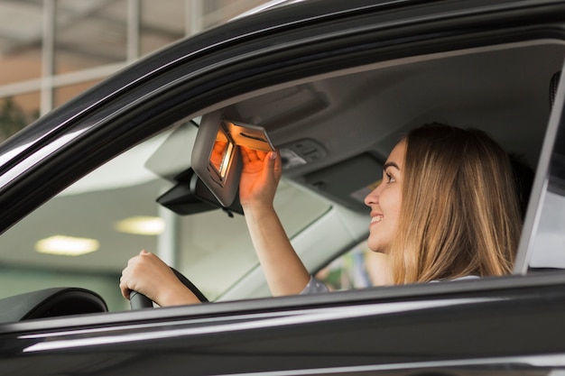 Glimlachende vrouw die in een autospiegel kijkt