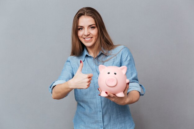 Glimlachende Vrouw die in overhemd moneybox ter beschikking houden