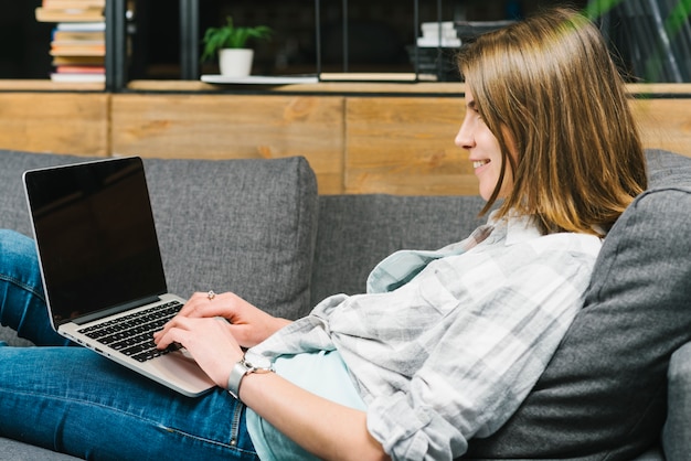 Glimlachende vrouw die laptop op bank met behulp van