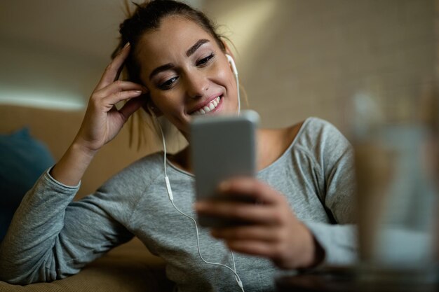Glimlachende vrouw die mobiele telefoon gebruikt en sms leest terwijl ze thuis ontspant