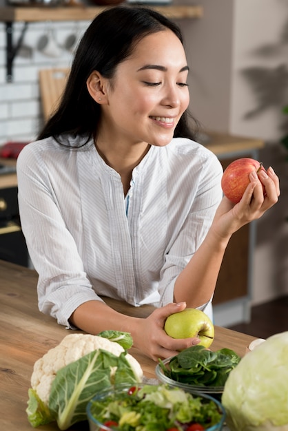 Glimlachende vrouw die rode appel in keuken thuis bekijkt