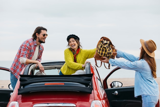 Gratis foto glimlachende vrouw die rugzak geeft aan dame die dichtbij de mens uit auto leunt