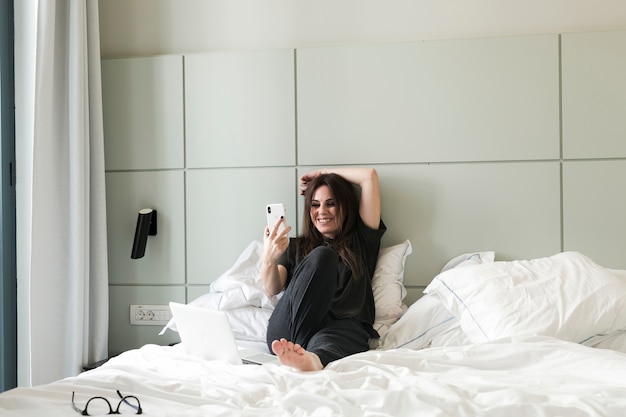 Glimlachende vrouw die selfie op bed nemen