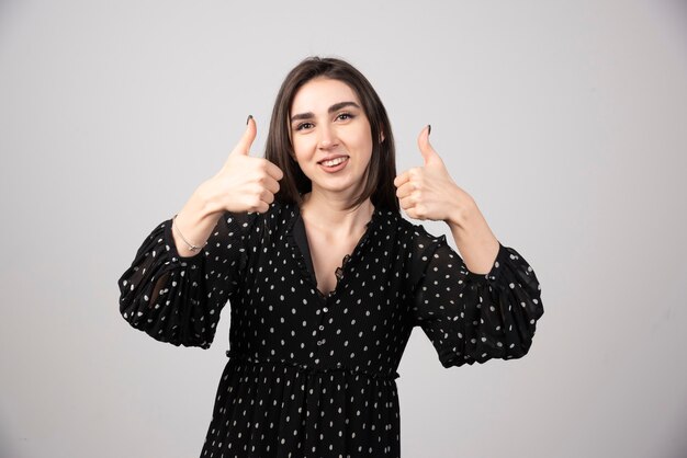 Glimlachende vrouw duimen opdagen en kijken naar de camera over grijze achtergrond.