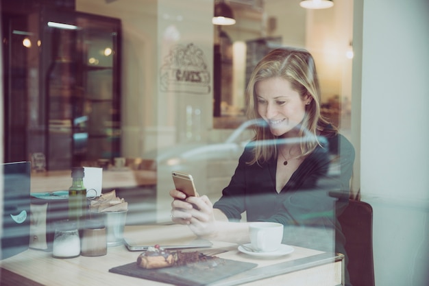 Glimlachende vrouw het doorbladeren smartphone in comfortabele koffie