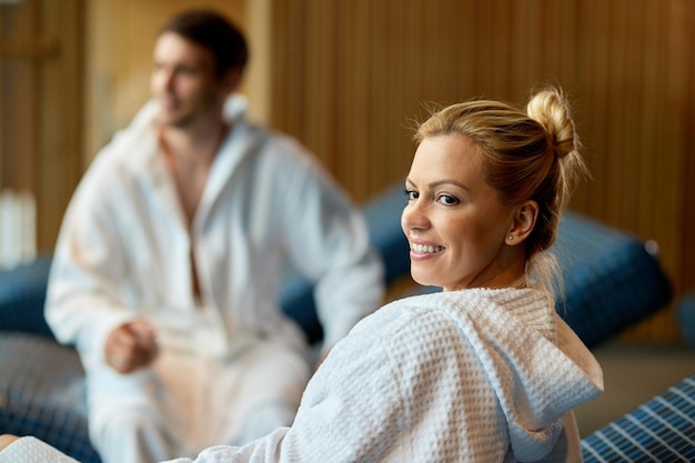 Glimlachende vrouw in badjas en haar man genieten van een dag in het wellnesscentrum