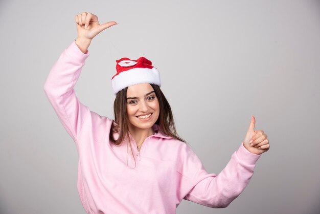 Glimlachende vrouw in de hoed van de Kerstman duimen opdagen.