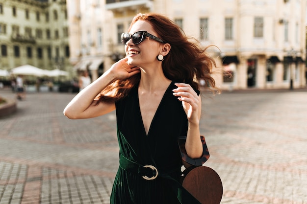 Glimlachende vrouw in donkergroene outfit geniet van stadswandeling
