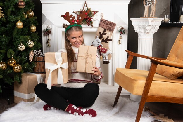 Glimlachende vrouw in hertenoren die twee kerstcadeautjes houden.