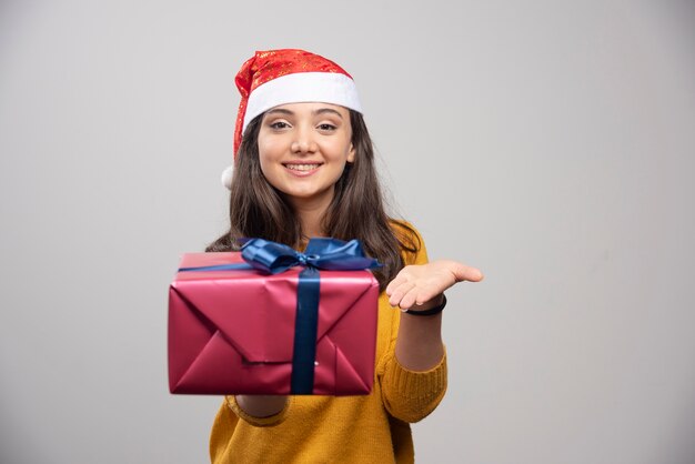 Glimlachende vrouw in Kerstmanhoed die een giftdoos toont.