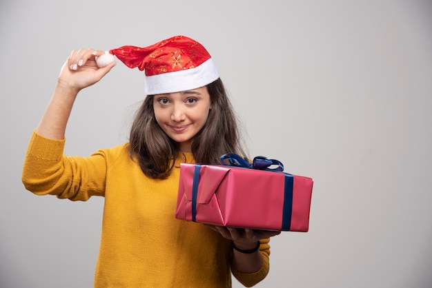 Glimlachende vrouw in kerstmanhoed die een giftdoos toont.