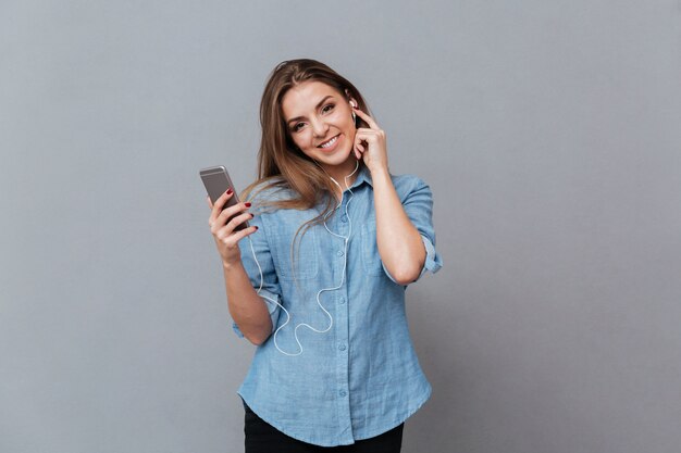 Glimlachende Vrouw in overhemd het luisteren muziek op telefoon