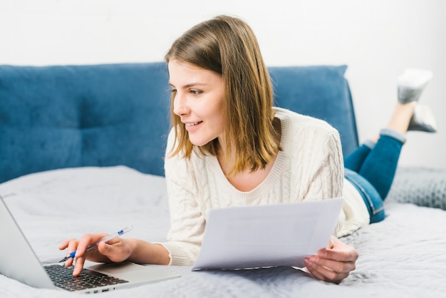 Glimlachende vrouw met documenten die laptop met behulp van