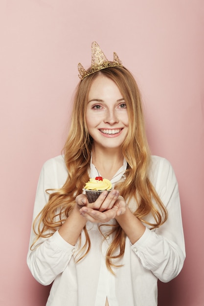 Gratis foto glimlachende vrouw, met een kroon, die een verjaardag houdt cupcake