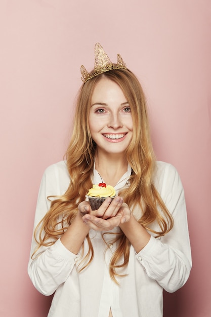 Glimlachende vrouw, met een kroon, die een verjaardag houdt cupcake
