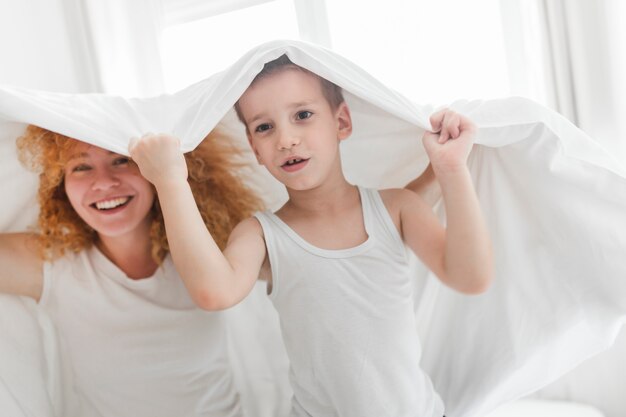 Glimlachende vrouw met haar zoon onder bedsheet