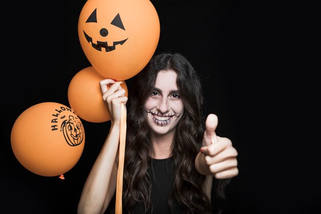 Glimlachende vrouw met Halloween-ballons die goed teken tonen