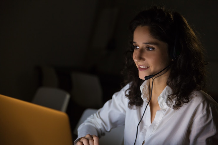 Gratis Foto glimlachende vrouw met hoofdtelefoon in donker bureau