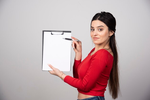 Glimlachende vrouw met lang haar die een klembord met potlood toont.