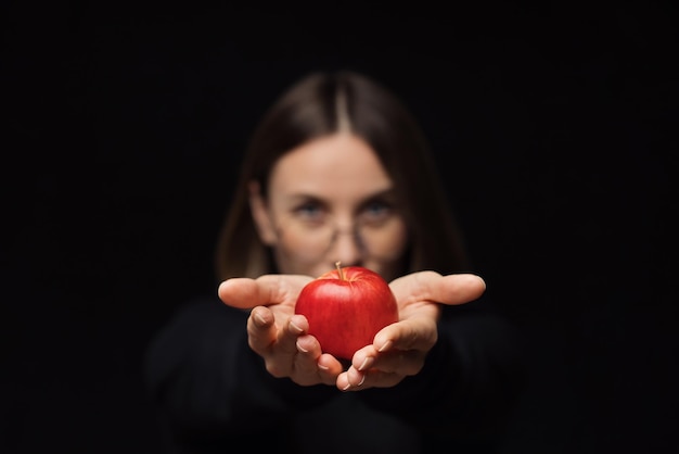 Glimlachende vrouw toont een appel aan de camera, met een bril op een zwarte achtergrond