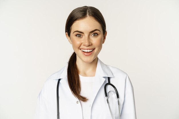 Glimlachende vrouwelijke arts-arts op afspraak die er gelukkig en zelfverzekerd uitziet met een witte jas en ste...