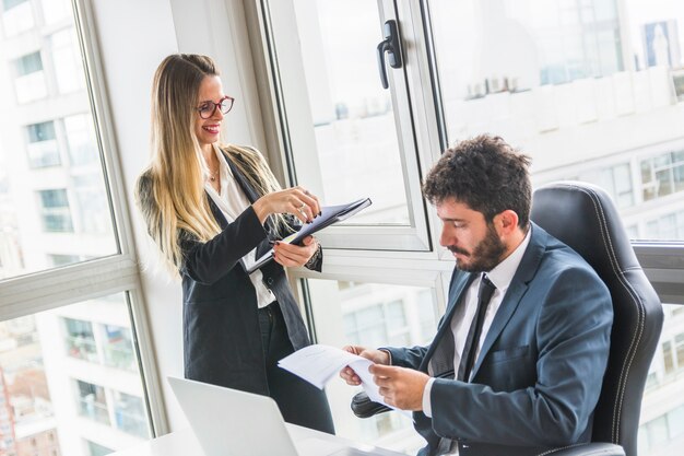 Glimlachende vrouwelijke secretaresse die zich dichtbij het mannelijke document van de managerlezing bevindt