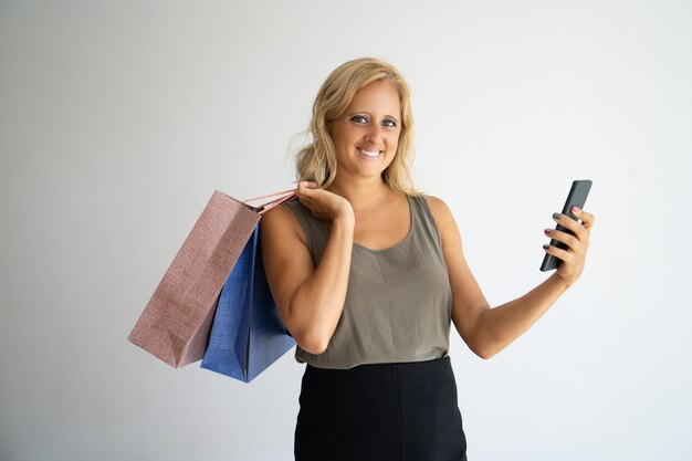 Glimlachende vrouwelijke shopaholic die smartphone gebruiken.