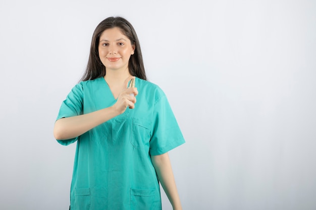 Glimlachende vrouwelijke verpleegster die nevelfles op wit toont.