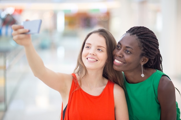 Glimlachende vrouwelijke vrienden binnenshuis zelfie nemen