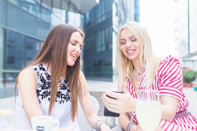 Glimlachende vrouwelijke vrienden die mobiele telefoon bekijken