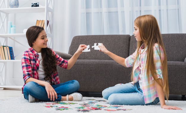 Glimlachende vrouwelijke vrienden die puzzelstuk thuis proberen te verbinden