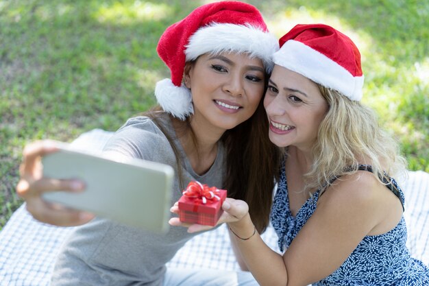 Glimlachende vrouwen die selfie foto met Kerstmisgift nemen in park