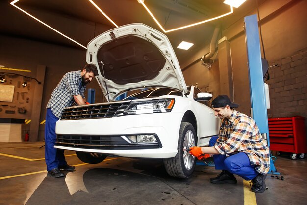 Glimlachende werktuigkundigen die moderne auto in workshop herstellen