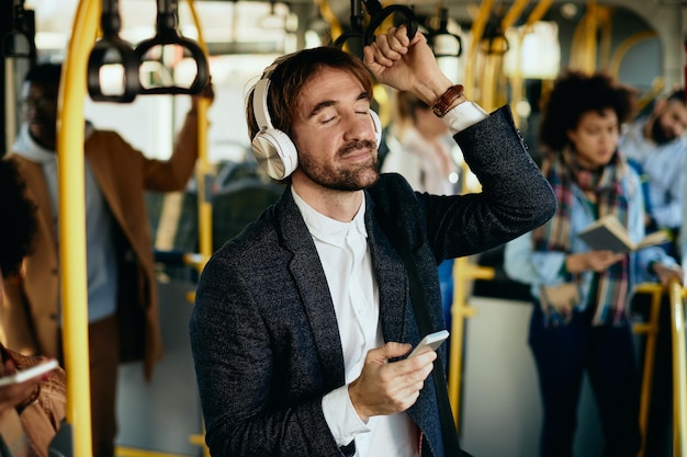 Glimlachende zakenman die muziek luistert met gesloten ogen tijdens het woon-werkverkeer met het openbaar vervoer