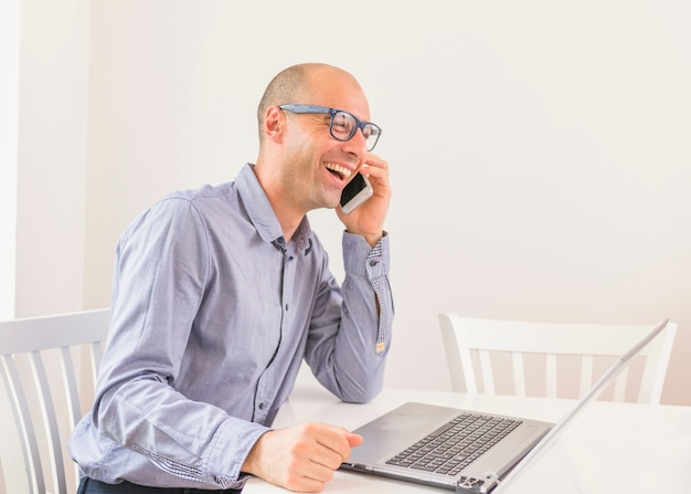 Glimlachende zakenman die op mobiele telefoon met laptop op lijst spreken