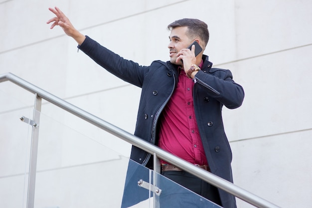 Glimlachende zakenman die op telefoon en groet spreekt