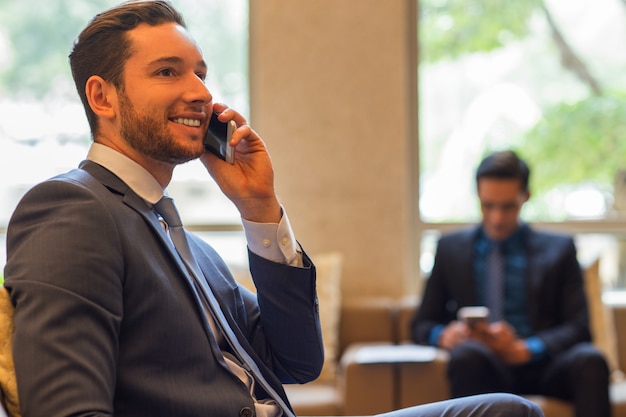 Glimlachende zakenman praten over de telefoon in de lounge