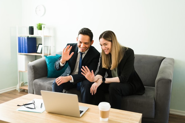 Glimlachende zakenpartners zwaaien en zeggen hallo tegen collega's en collega's tijdens een videogesprek op een laptop. Zakenvrouw en man tijdens een online vergadering op kantoor