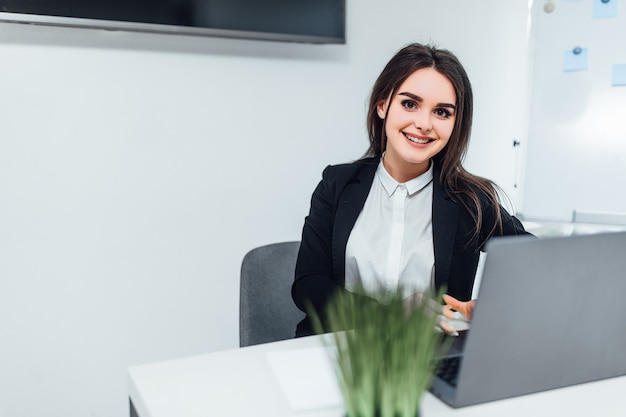 Glimlachende zakenvrouw gekleed casual pak zittend in een modern kantoor en met behulp van laptop. Met kopie ruimte.